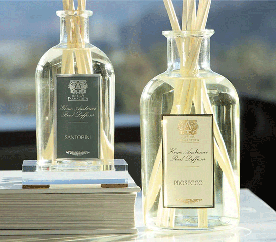 To bottles of Antica Farmacista against a background view out a window to nature.