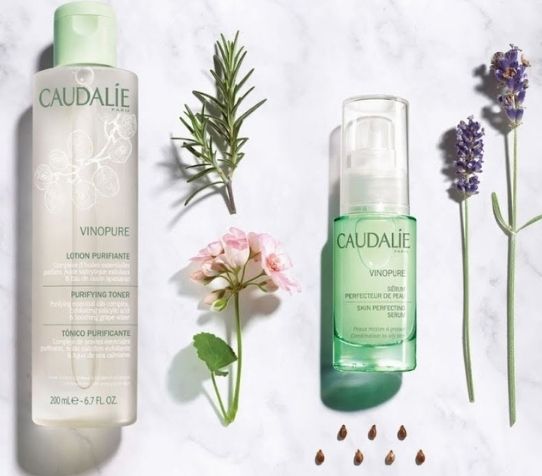 Two of Caudalie's Vinopure products surrounded with flowers and herbs.