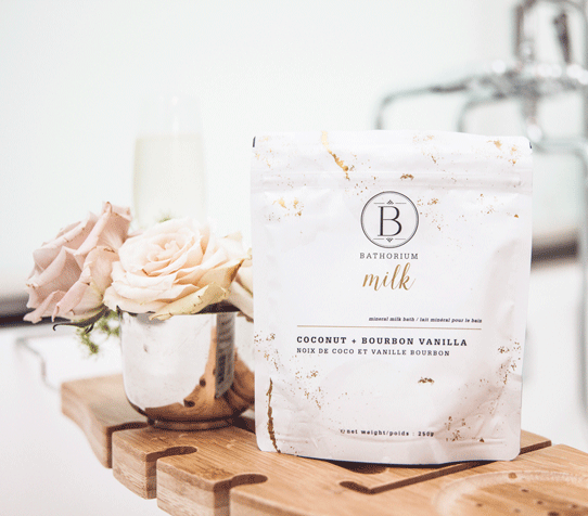 a bag of Coconut Bourbon Vanilla Milk Bath with two beige roses and bath accessories.