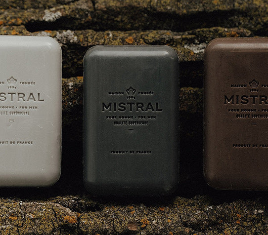 Three Mistral Men's Bar Soap on a dark stone.