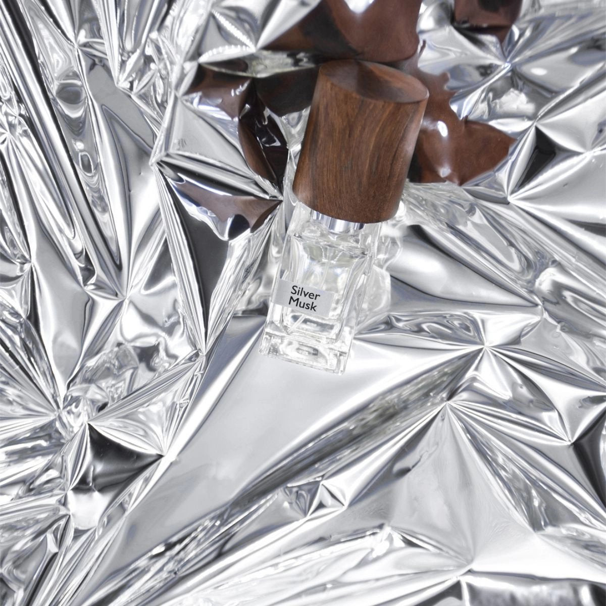 A bottle of nasomatto's Silver Musk Cologne on a bed of silver folded fabric