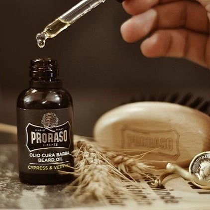 A bottle of Proraso's Cypress and Vetiver Beard Oils with a dropper.  I the background is a Proraso Beard Brush.