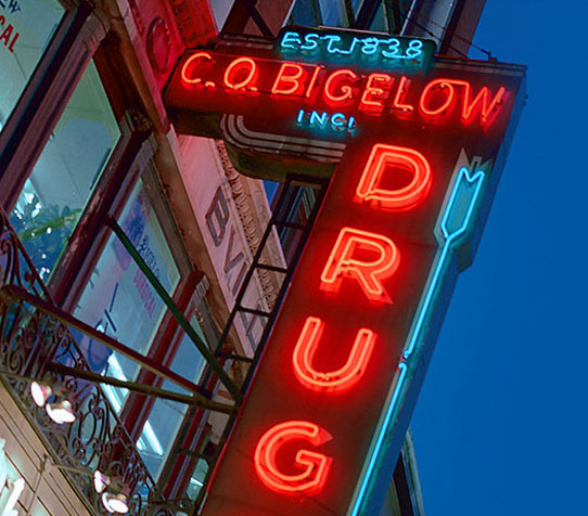 The neon sign that is hanging along the front of the Bigelow Store reading 'Est 1838 C.O. Bigelow Drugs Inc'