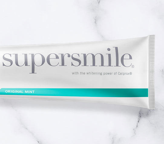 A partial photo of a Supersmile tube of Original Mint Toothpaste on a marble countertop background.