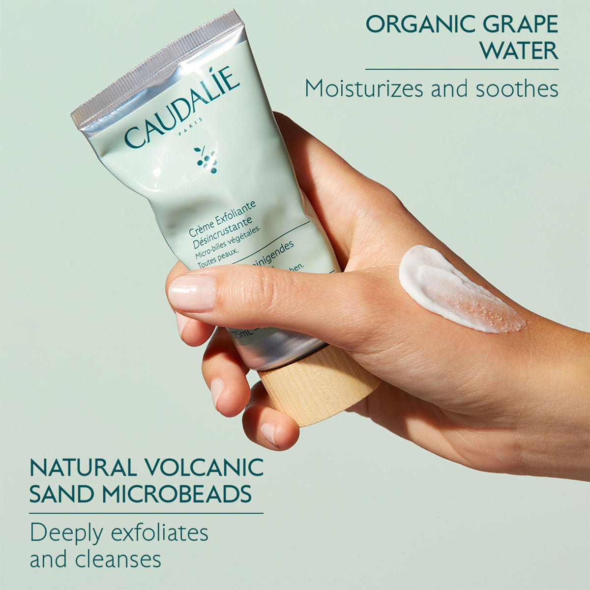 Hand holding a Caudalie skincare product with text about organic grape water and natural volcanic sand microbeads.