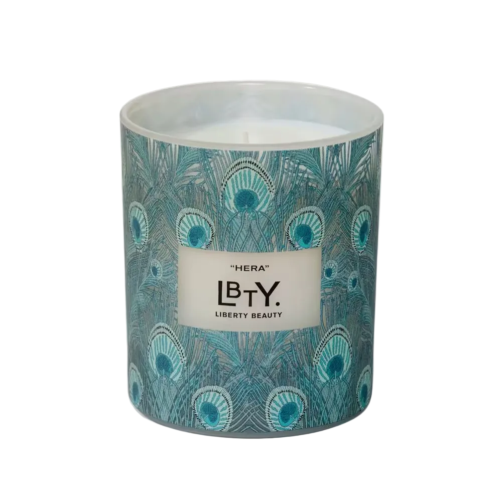 Candle with peacock feather design and 'Liberty Beauty' branding on a white background