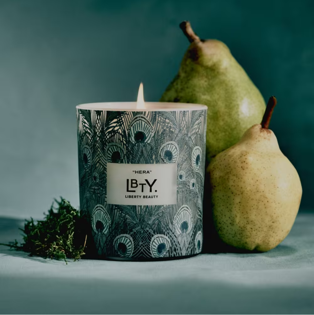 Candle with decorative label next to two pears on a green background