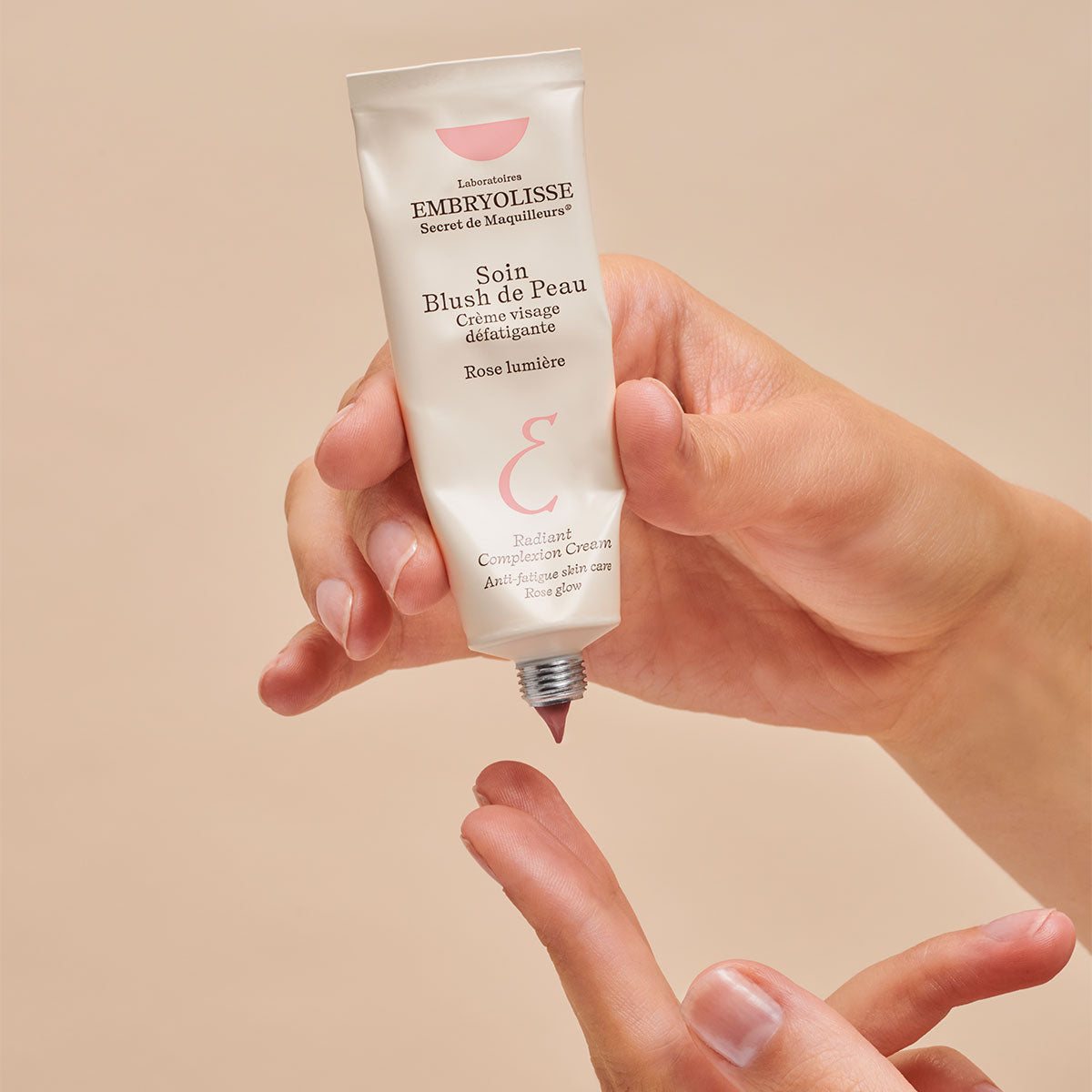 A person squeezing Embryolisse Radiant Complexion Cream in Rose Glow onto their fingers. 
