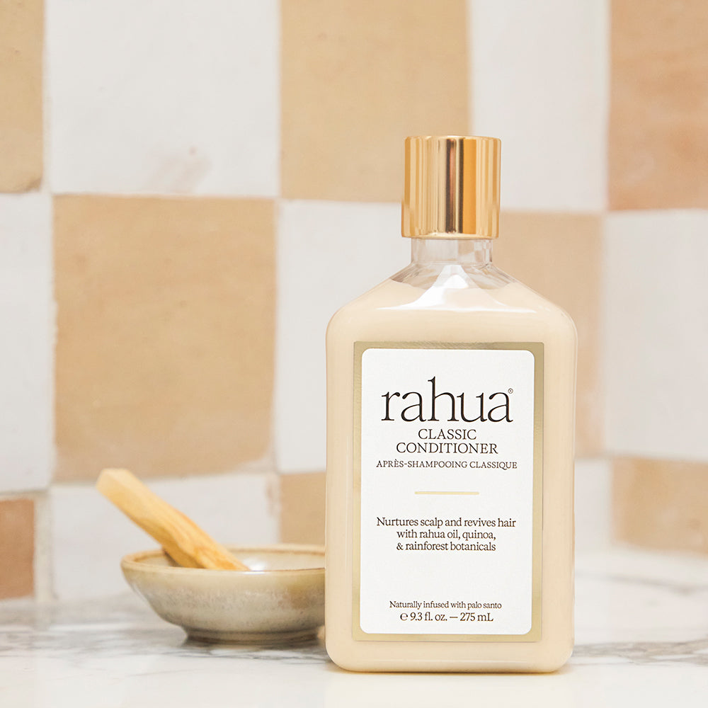 Bottle of rahua classic conditioner on a bathroom counter with a tiled wall background