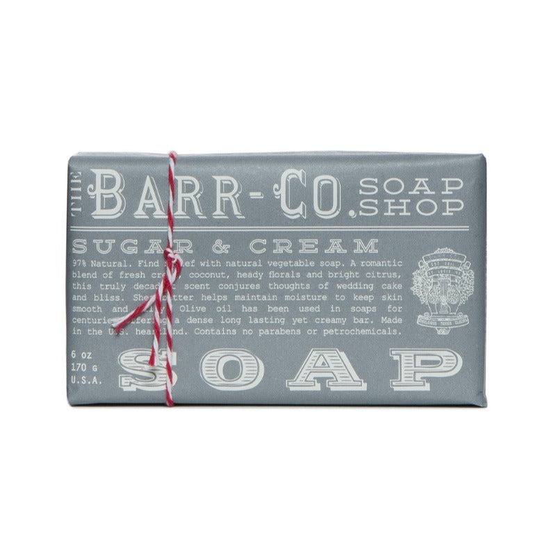 A gray bar of soap with 'BARR-Co SOAP SHOP SUGAR & CREAM' printed in white and red, sealed with a red twist tie.