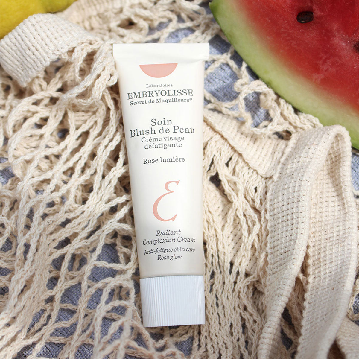 Embryolisse Radiant Complexion Cream in Rose Glow on a net next to a watermelon.