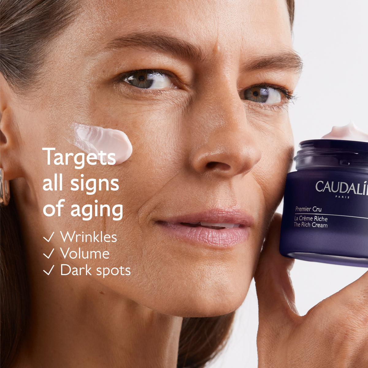 Woman holding a jar of Caudalie cream with text about anti-aging benefits on a white background