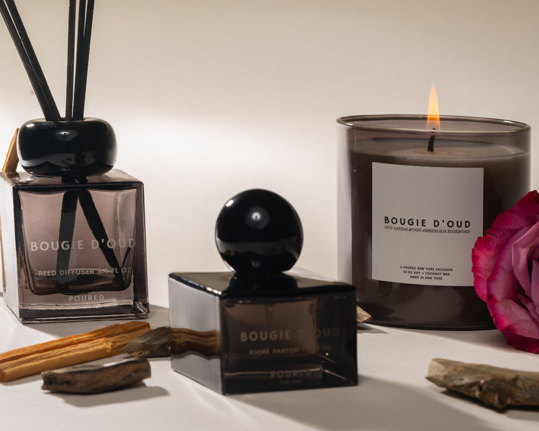 Bougie d'Oud candles and diffuser on a white surface with a pink flower.