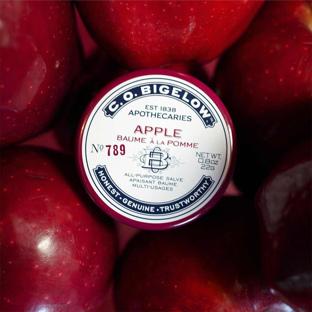C.O. Bigelow Apple All-Purpose Salve Tin surrounded by red apples.
