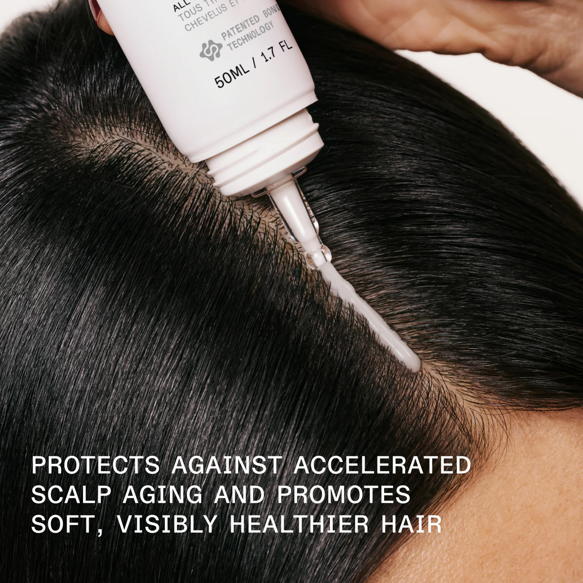 A close-up of a person's dark hair receiving a scalp treatment, with a white tube being squeezed to apply a white cream along the hairline. Text at the bottom reads, 'PROTECTS AGAINST ACCELERATED SCALP AGEING AND PROMOTES SOFT, VISIBLY HEALTHIER HAIR'.