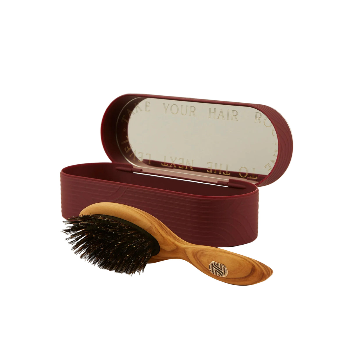 A wooden hairbrush with black bristles placed in front of an open oval burgundy case with a mirror inside, on a light beige background.