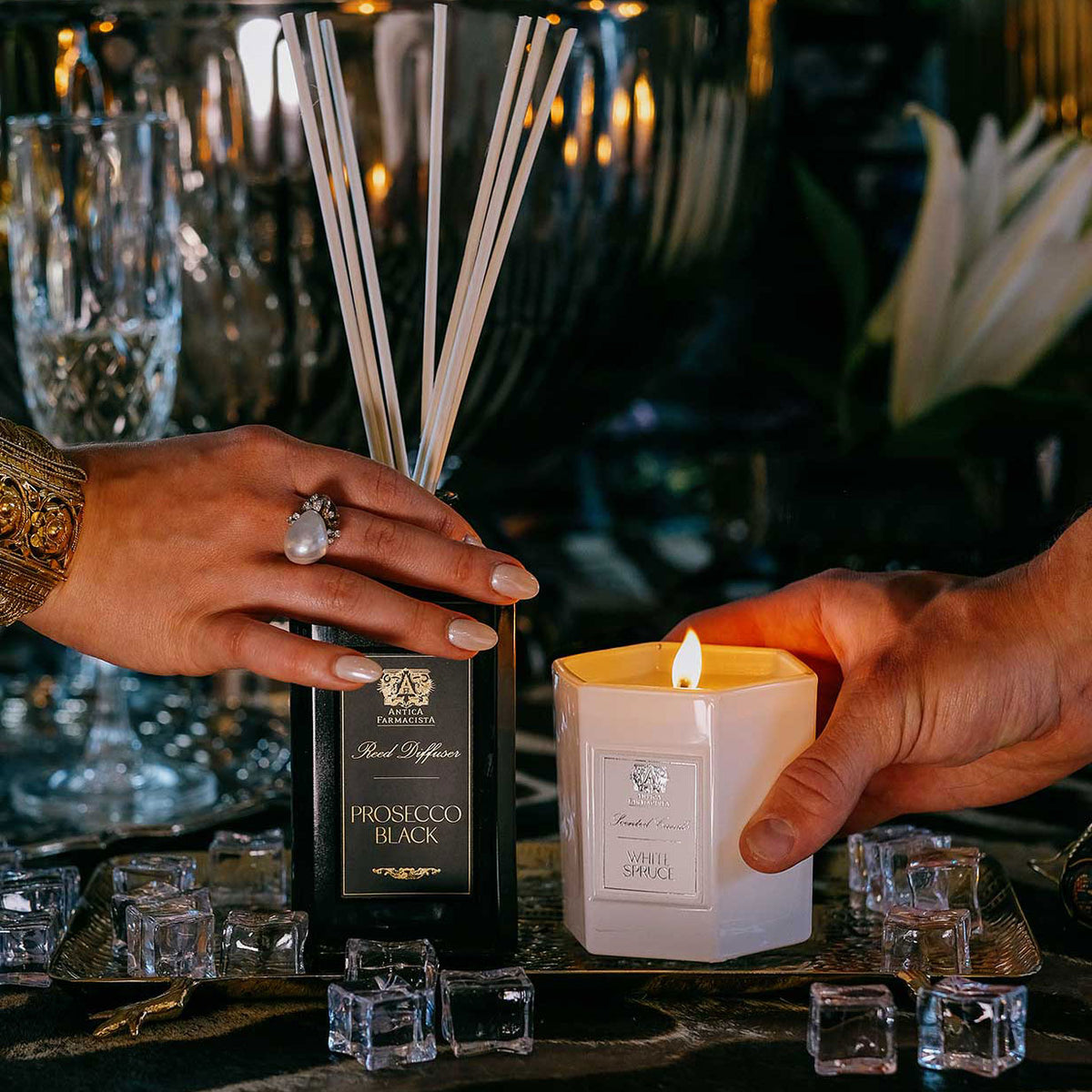 A hand holding diffuser and a hand holding a candle on a table with various dinner party objects.