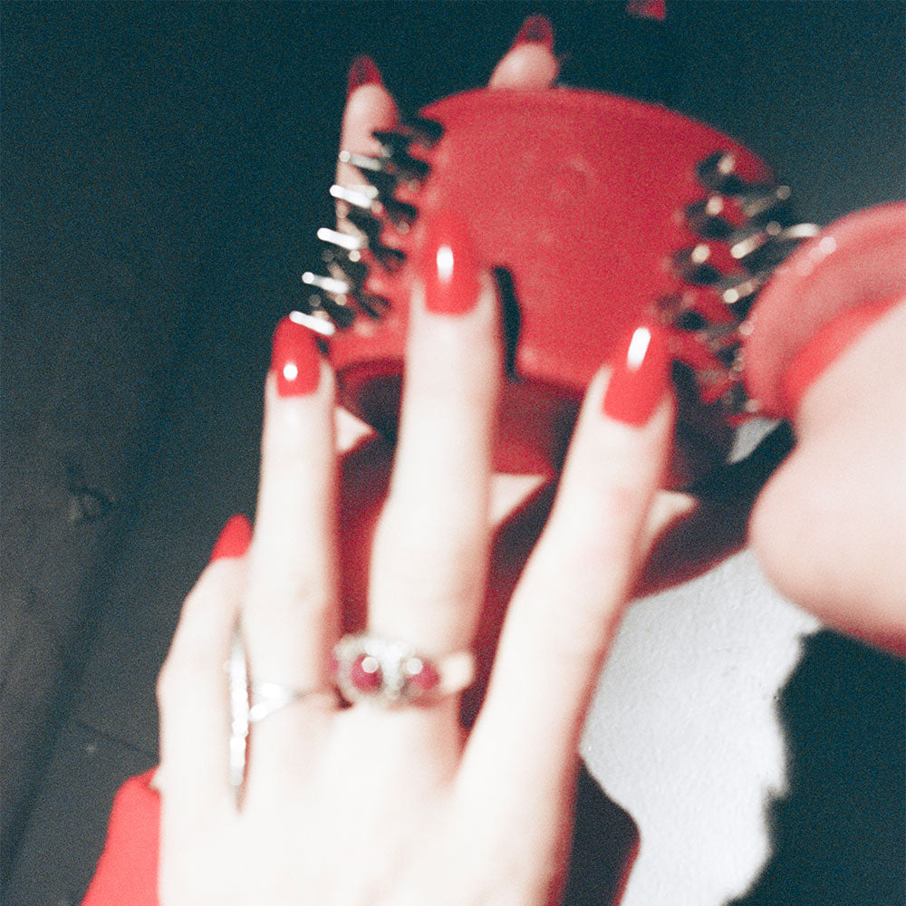Hands holding red and spiked bracelet over a dark industrial background