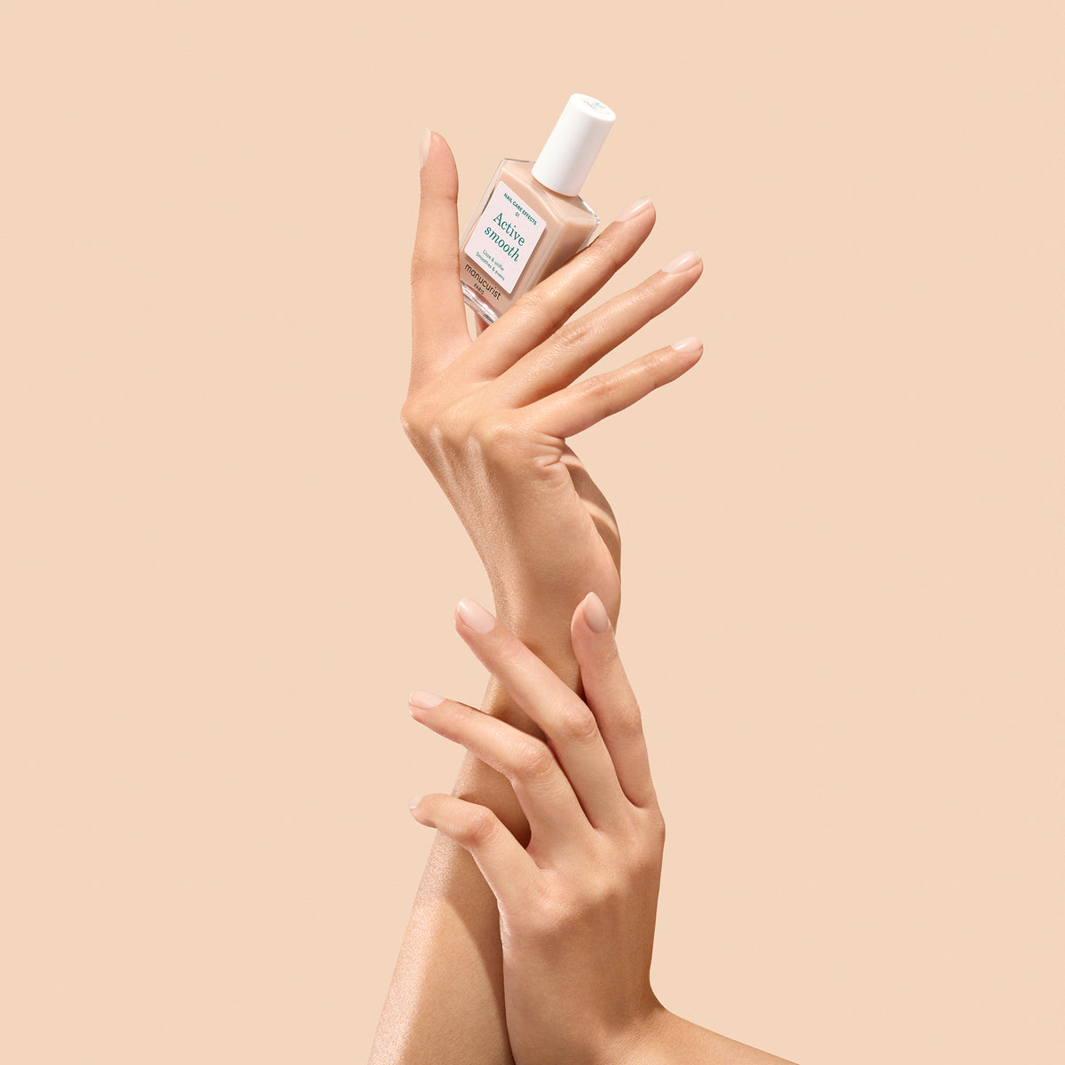 Hand holding a bottle Manucrurist Active Smooth 01 against a beige background