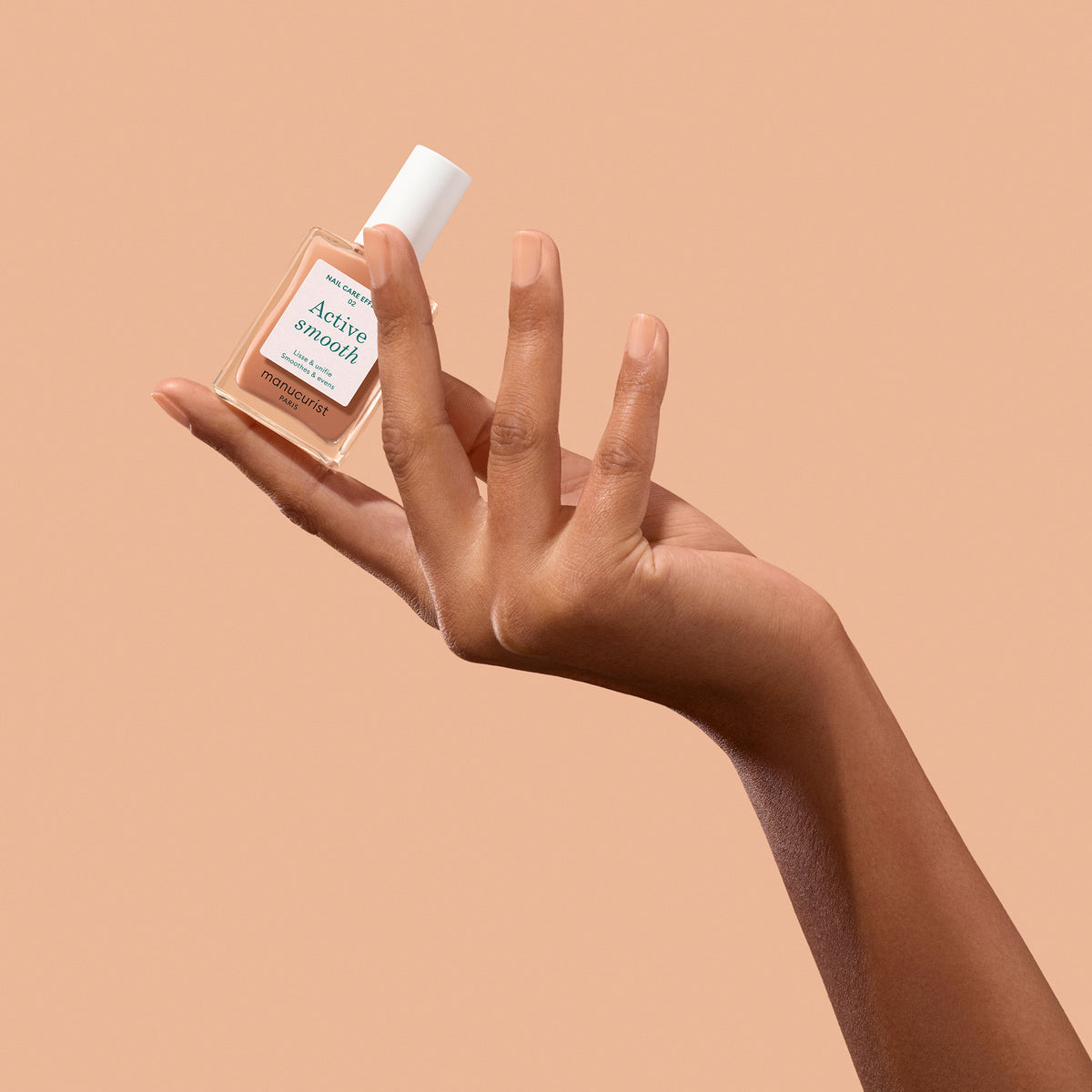 Manucurist Active smooth on models hand while holding bottle on tan background  