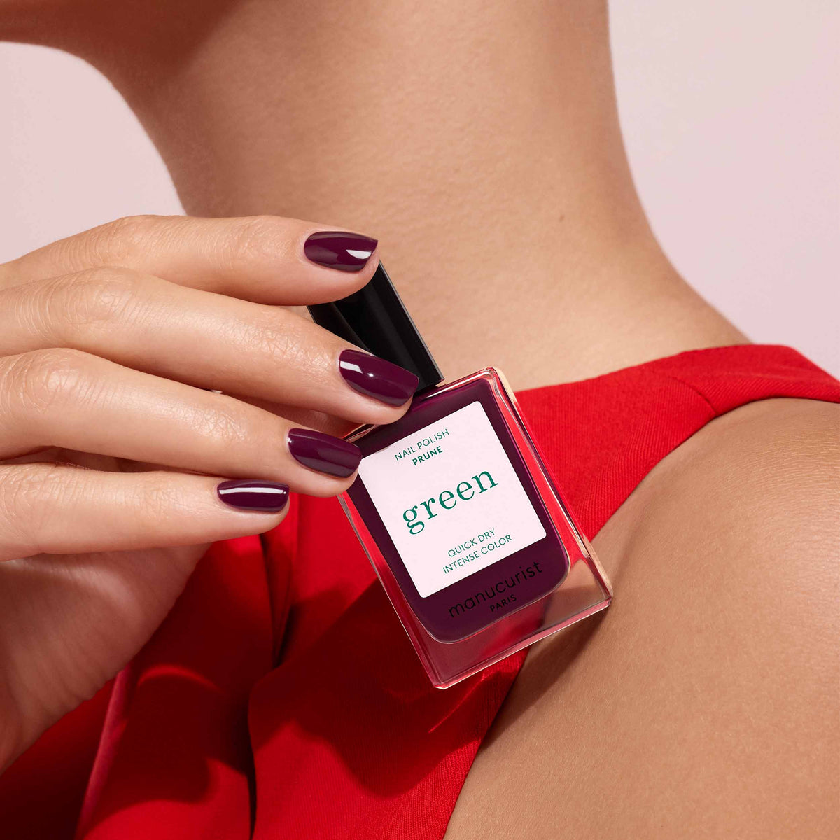 Hand holding a perfume bottle labeled  Prune with a red dress and pink background