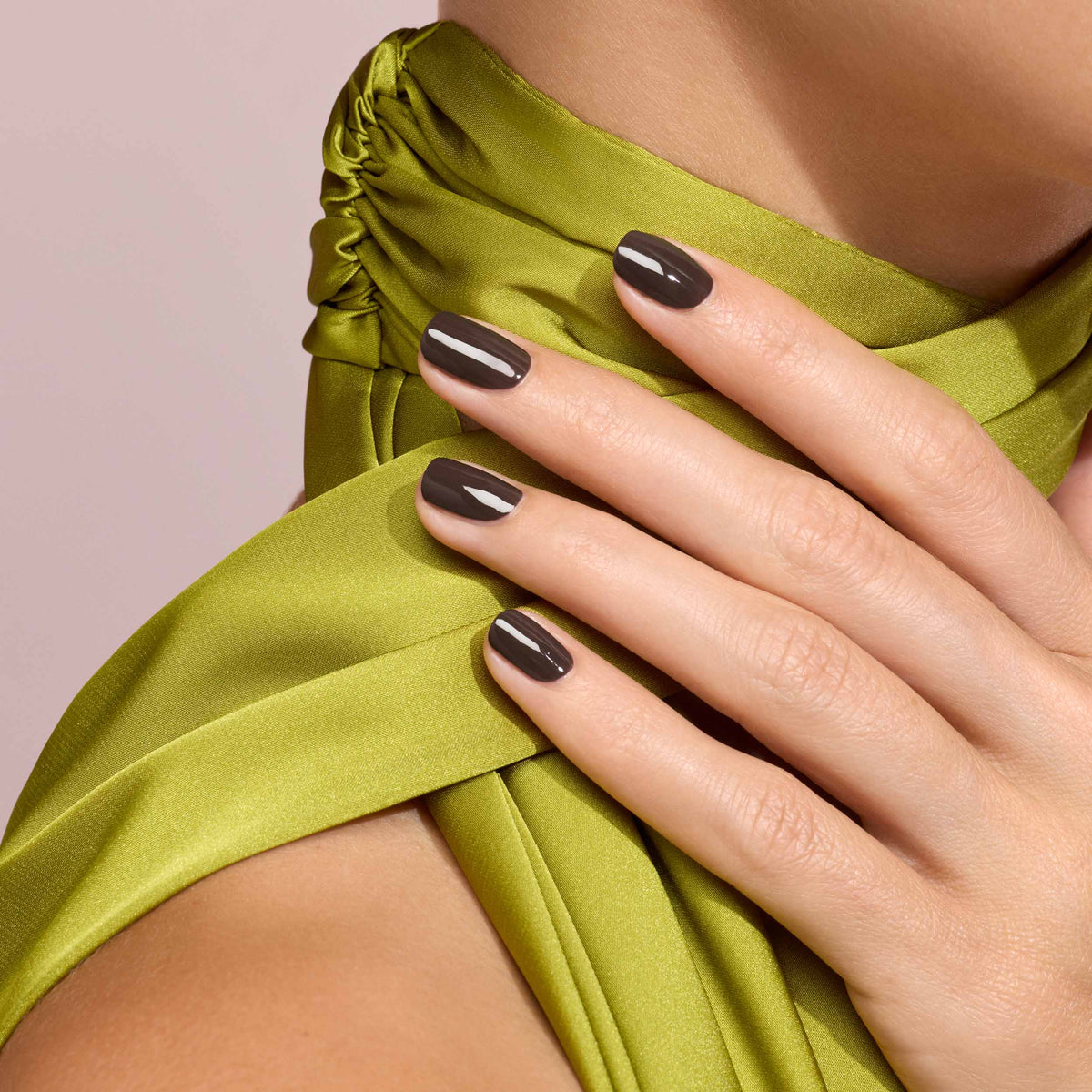 Close-up of a hand with dark nail polish on a green garment against a pink background