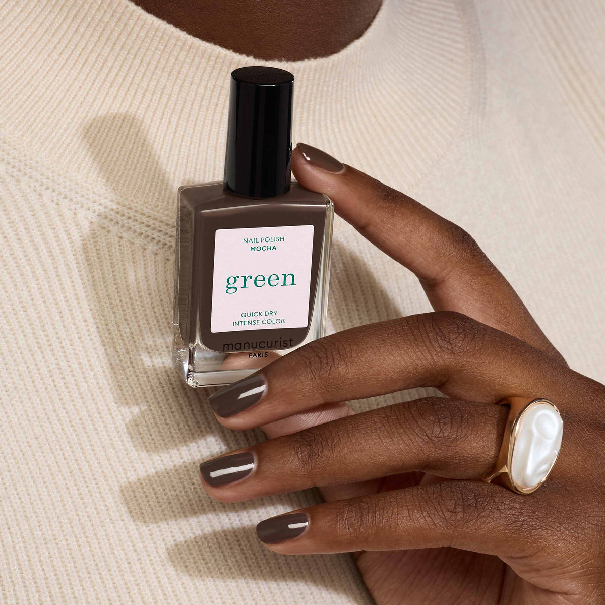 Hand holding a bottle of Manucurist Mocha nail polish with a visible brand label on a neutral background