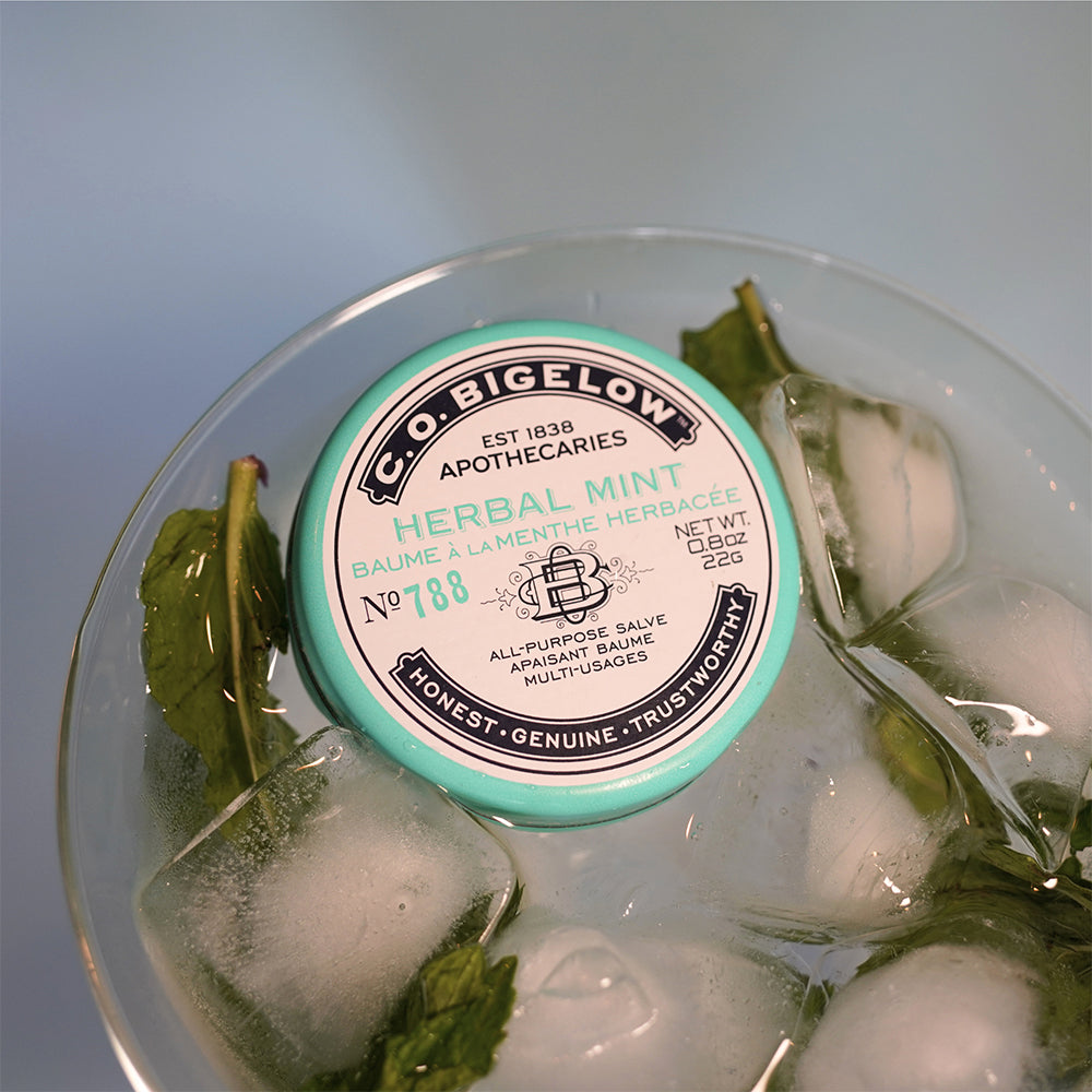 C.O. Bigelow Herbal Mint salve container in a glass of ice with Mint leaves. 