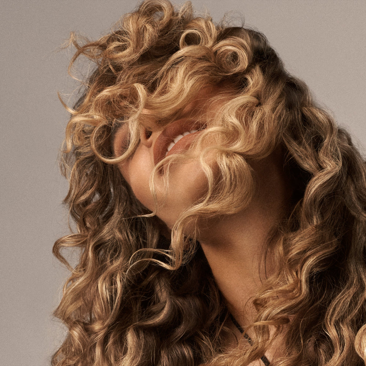 Close-up of a person with voluminous, wavy hair on a neutral background