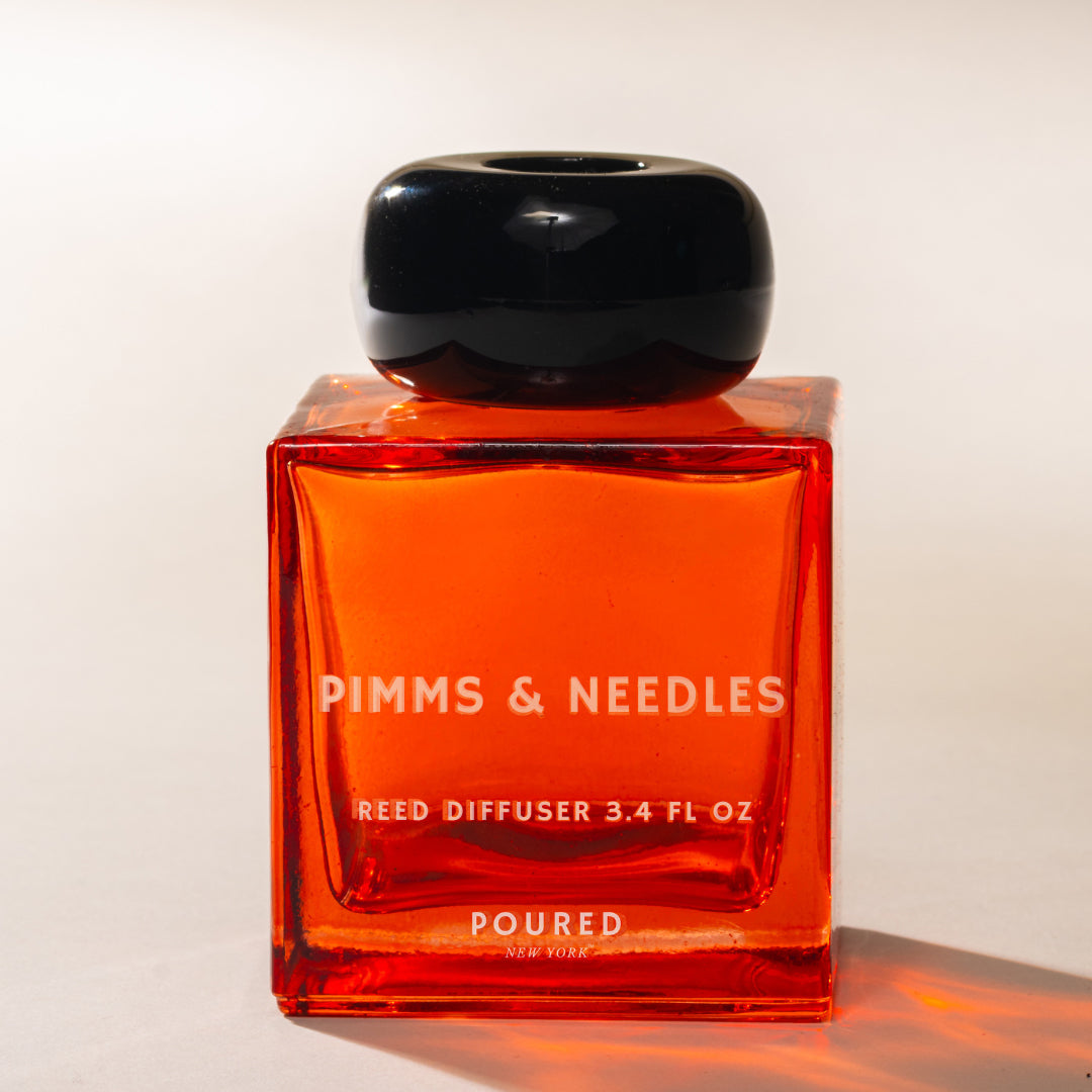 Red reed diffuser with black cap labeled 'Pimms & Needles' on a neutral background