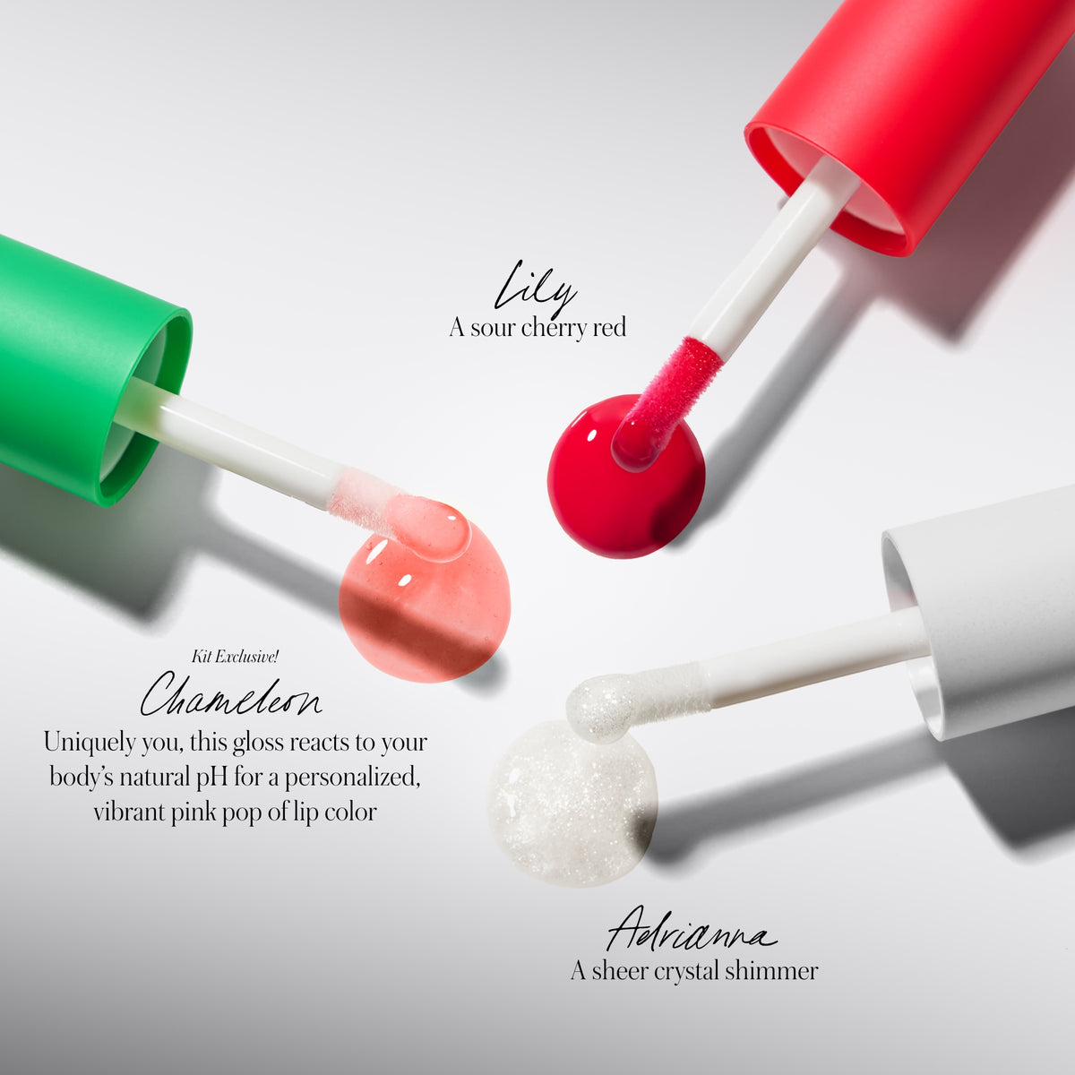 Three lip glosses with red, green, and white caps on a light gray background.