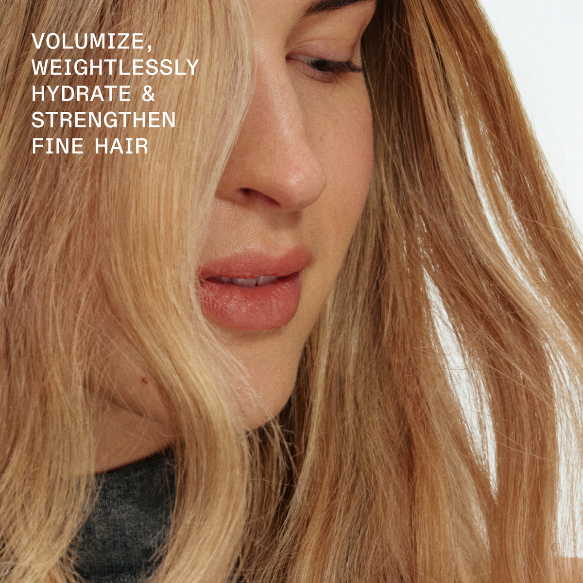 Close-up of a woman with long blonde hair wearing a dark gray top, with white text in the upper left reading 'VOLUMIZE, WEIGHTLESSLY HYDRATE & STRENGTHEN FINE HAIR' against a plain light background.