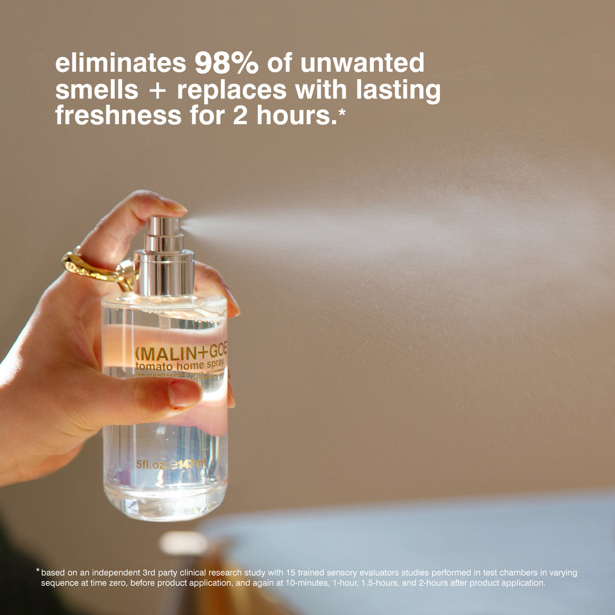 Hand holding a spray bottle with text about eliminating smells and lasting freshness.