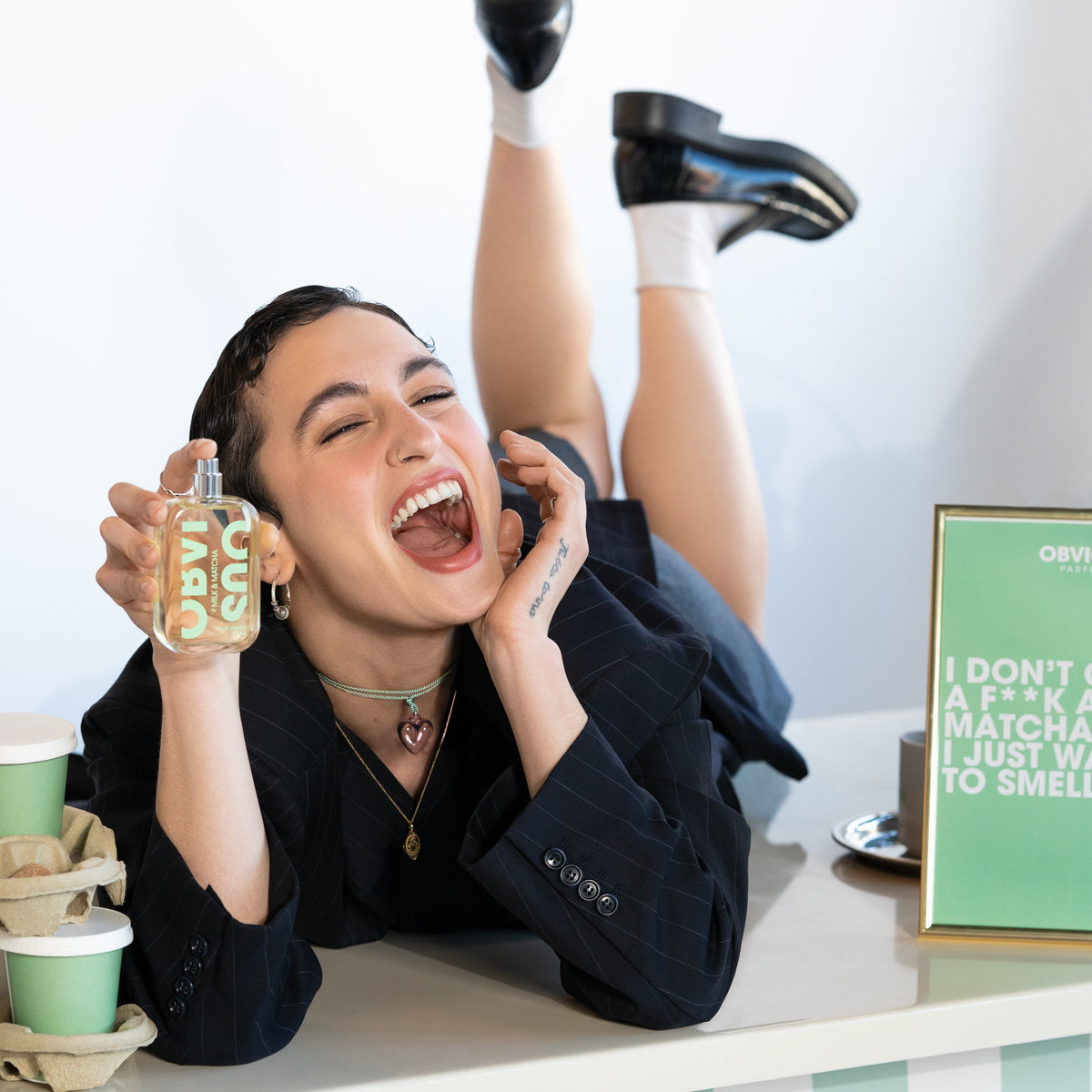 Person holding a bottle of perfume with a checkered floor and green sign in the background