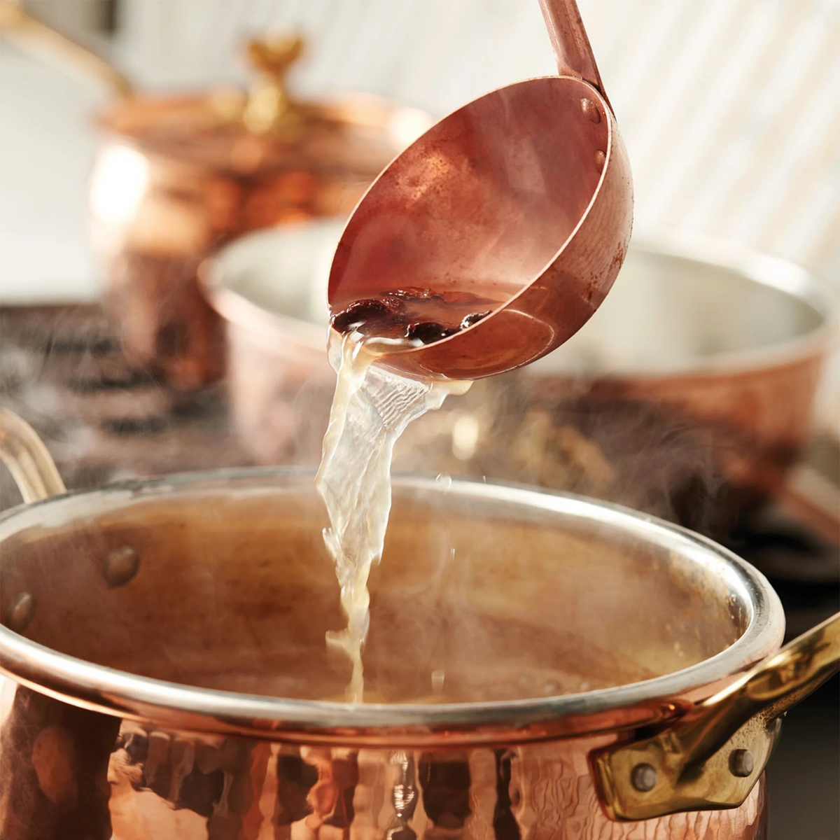 Copper ladle lifting a steaming bowl of soup from a copper pot.