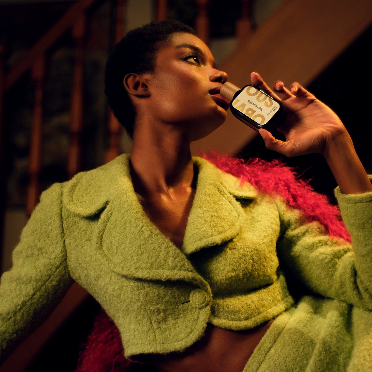 Woman in a green coat holding a perfume bottle with a blurred background