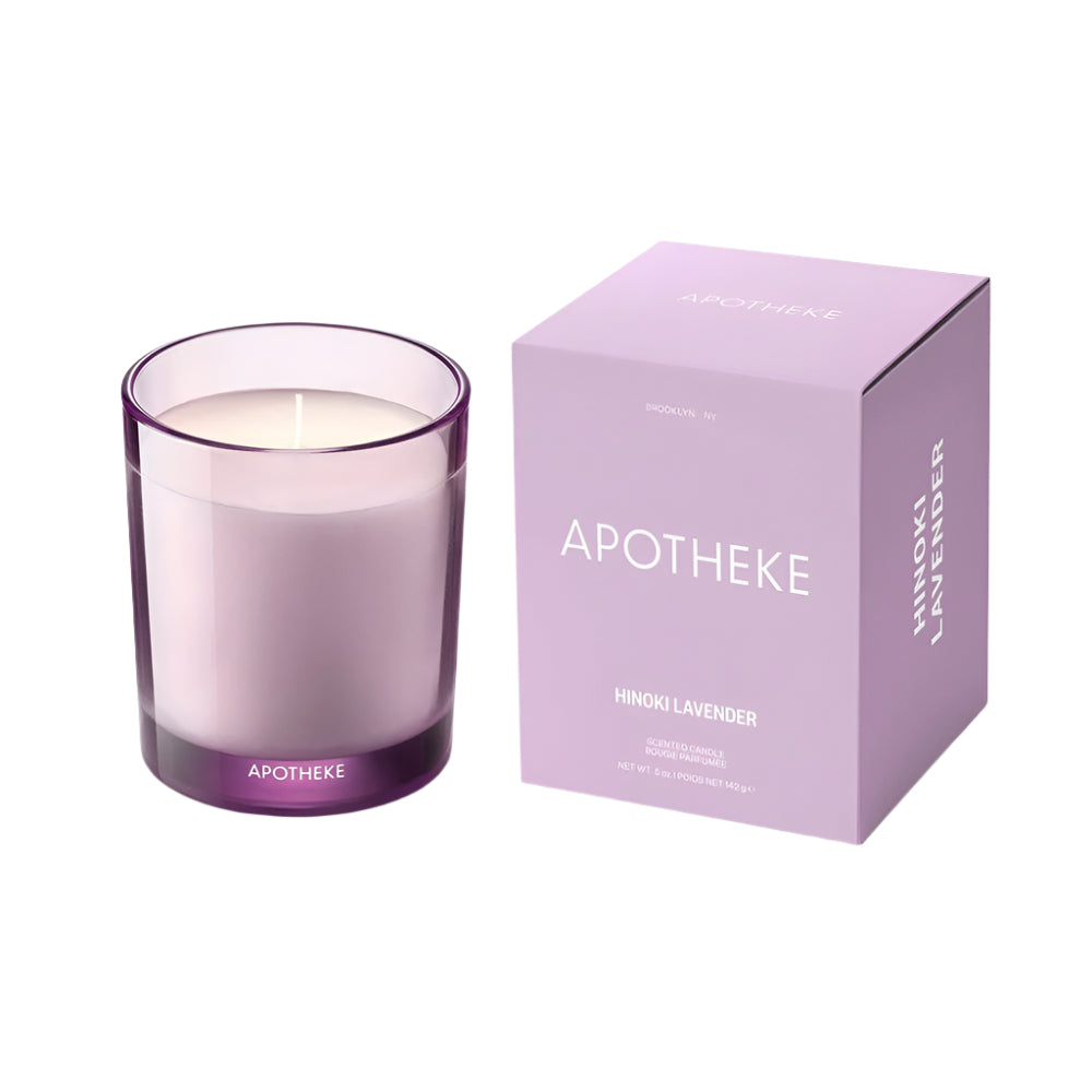 A Hinoki Lavender scented candle by Apotheke, shown in a clear glass jar with a purple lid, matching the box it comes in. The packaging box is purple with the brand name and product title.