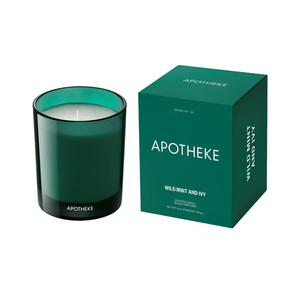 A green soy wax candle with a white wick, in a clear glass jar with a dark green lid, labeled 'APOTHEKE WILD MINT AND IVY'. The product is displayed alongside a matching green box with the brand name and product title.