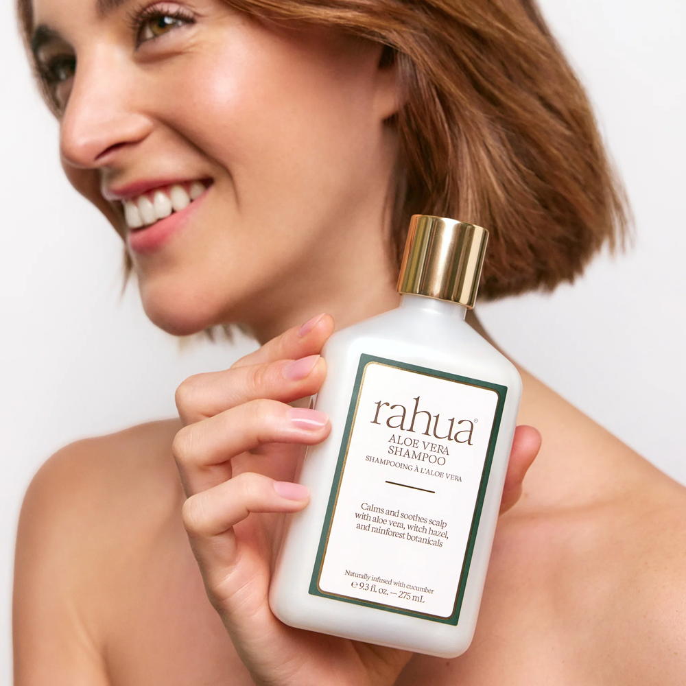 Woman holding a bottle of Rahua Aloe Vera Shampoo in front of a white background