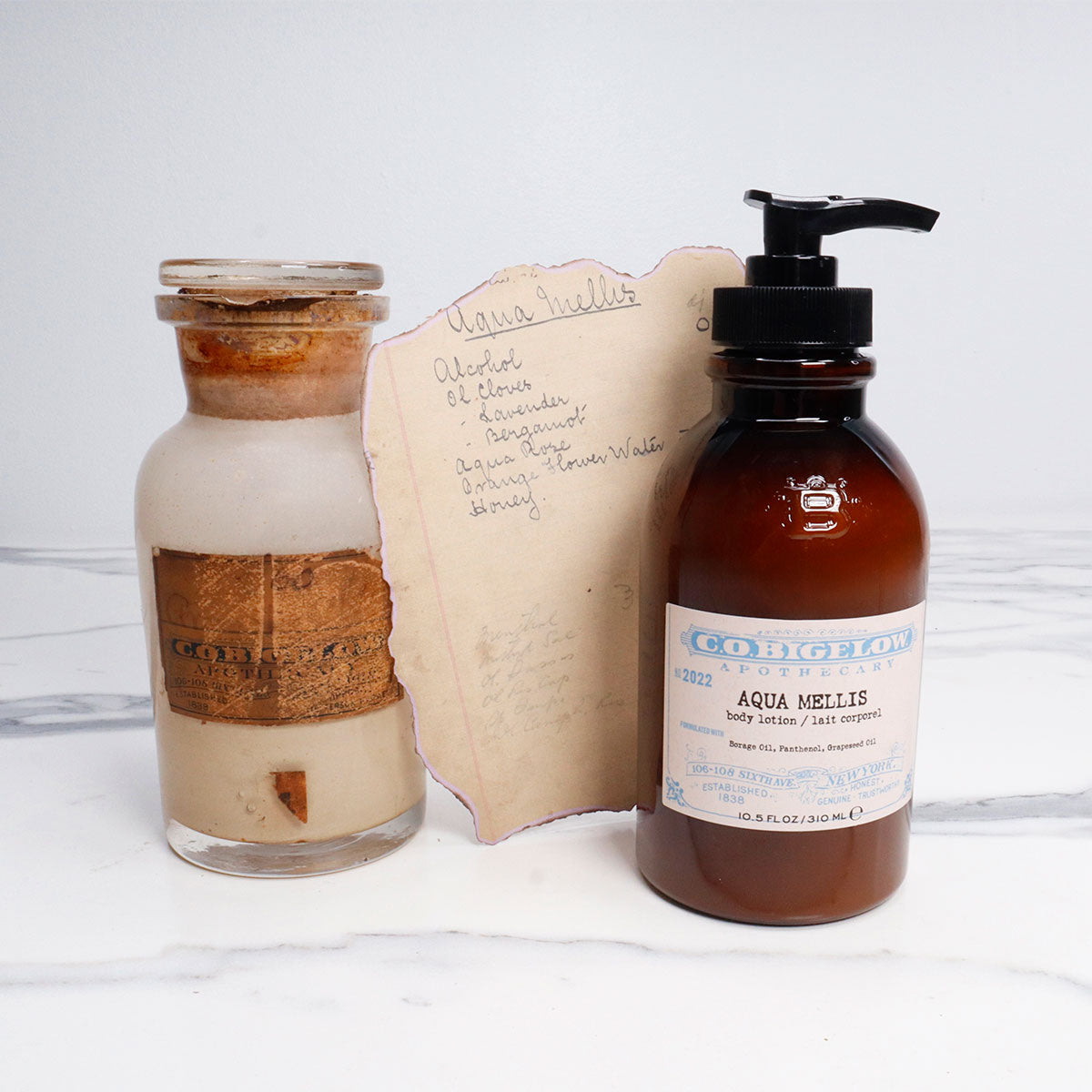 C.O. Bigelow Aqua Mellis Body Lotion in an amber bottle next to the original C.O. Bigelow Aqua Mellis formulary and apothecary Jar. 
