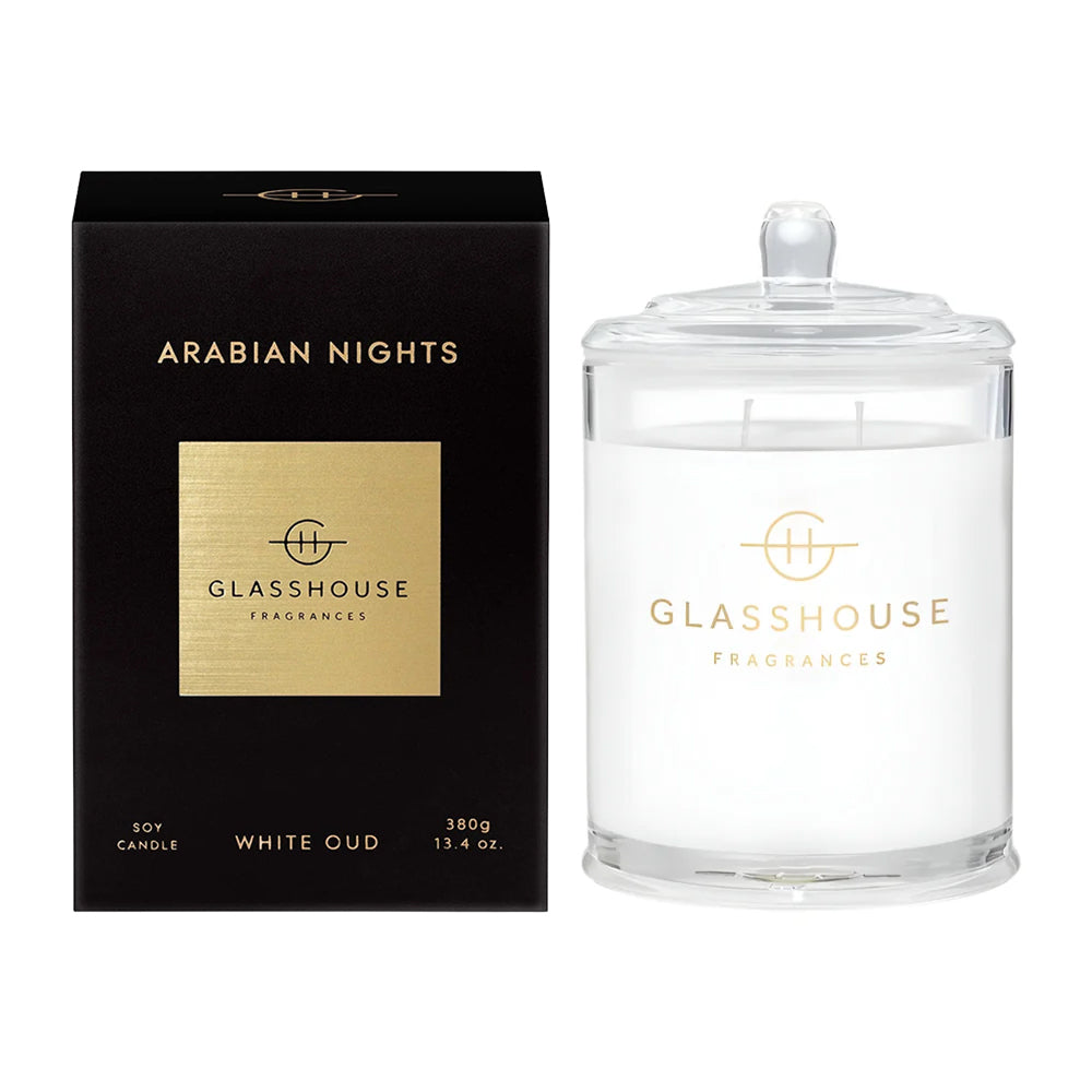 A luxury soy candle in a clear glass jar with a glass lid, shown next to its black packaging box. The box features a metallic gold square with the brand name 'GLASSHOUSE FRAGRANCES' and the scent name 'ARABIAN NIGHTS'.