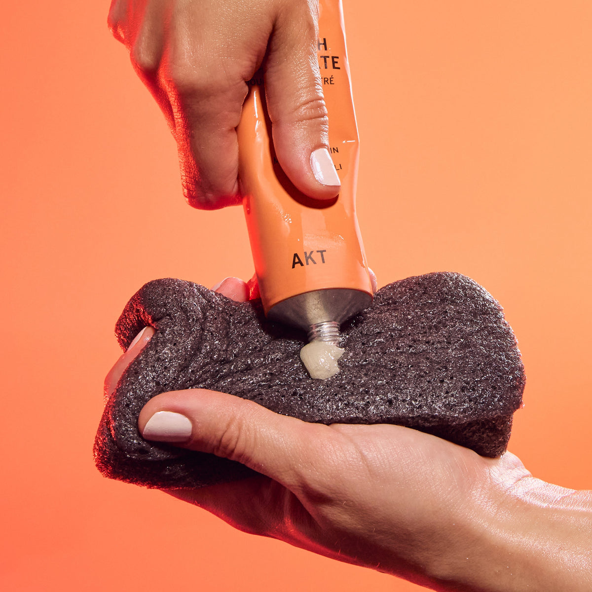Hand squeezing AKT's Body Wash Concentrate onto AKT's Konjac Sponge held by their other hand. 