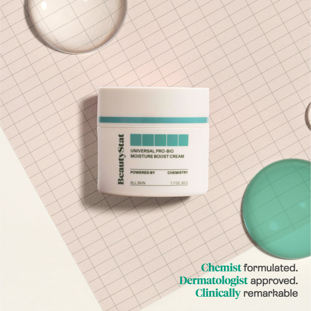 Tub of 'Universal Pro-Bio Moisture Boost Cream' on a gridded background next to large droplets of liquid.