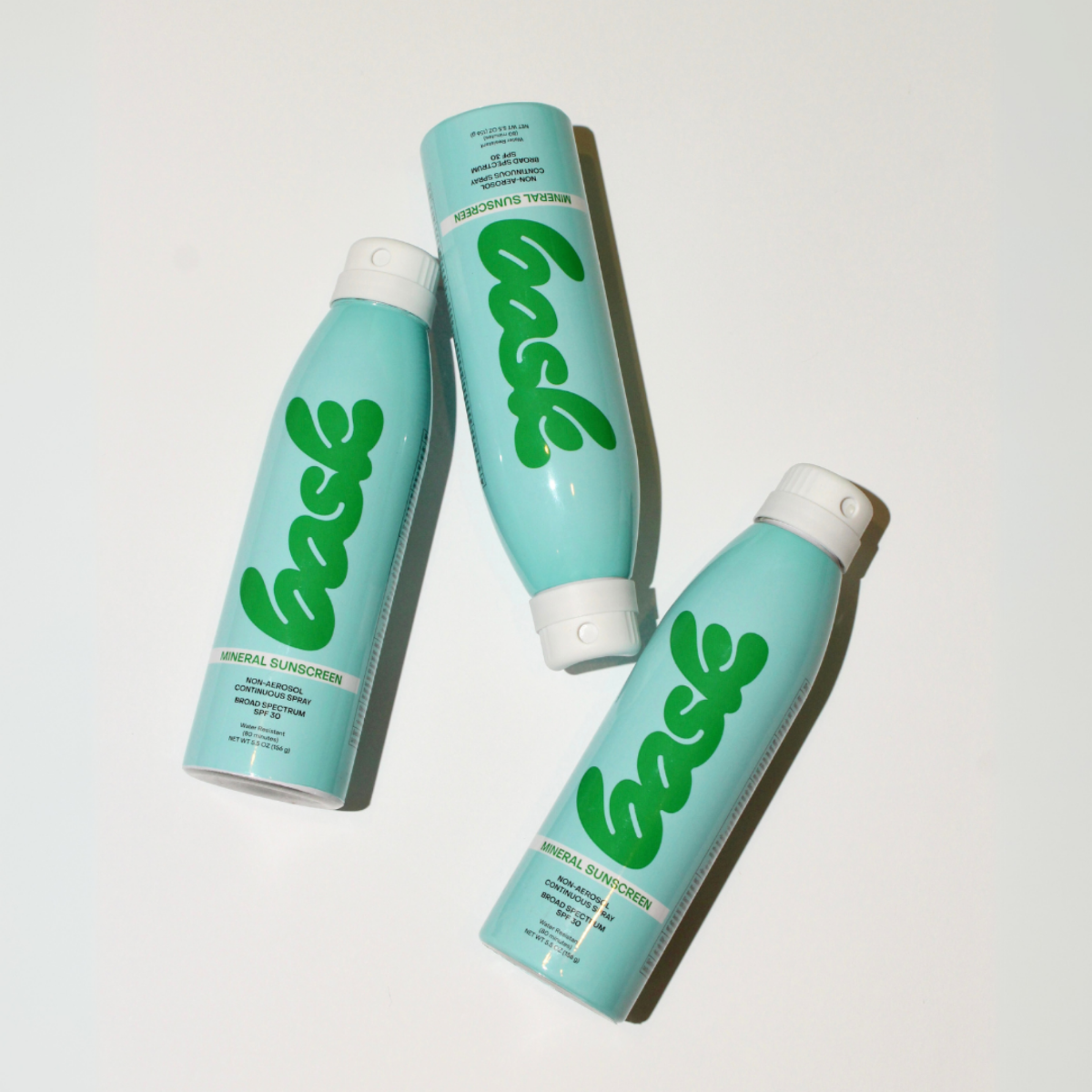 Three bottles of Bask's mineral sunscreen on a flat white surface. Bottles are blue with green text. 
