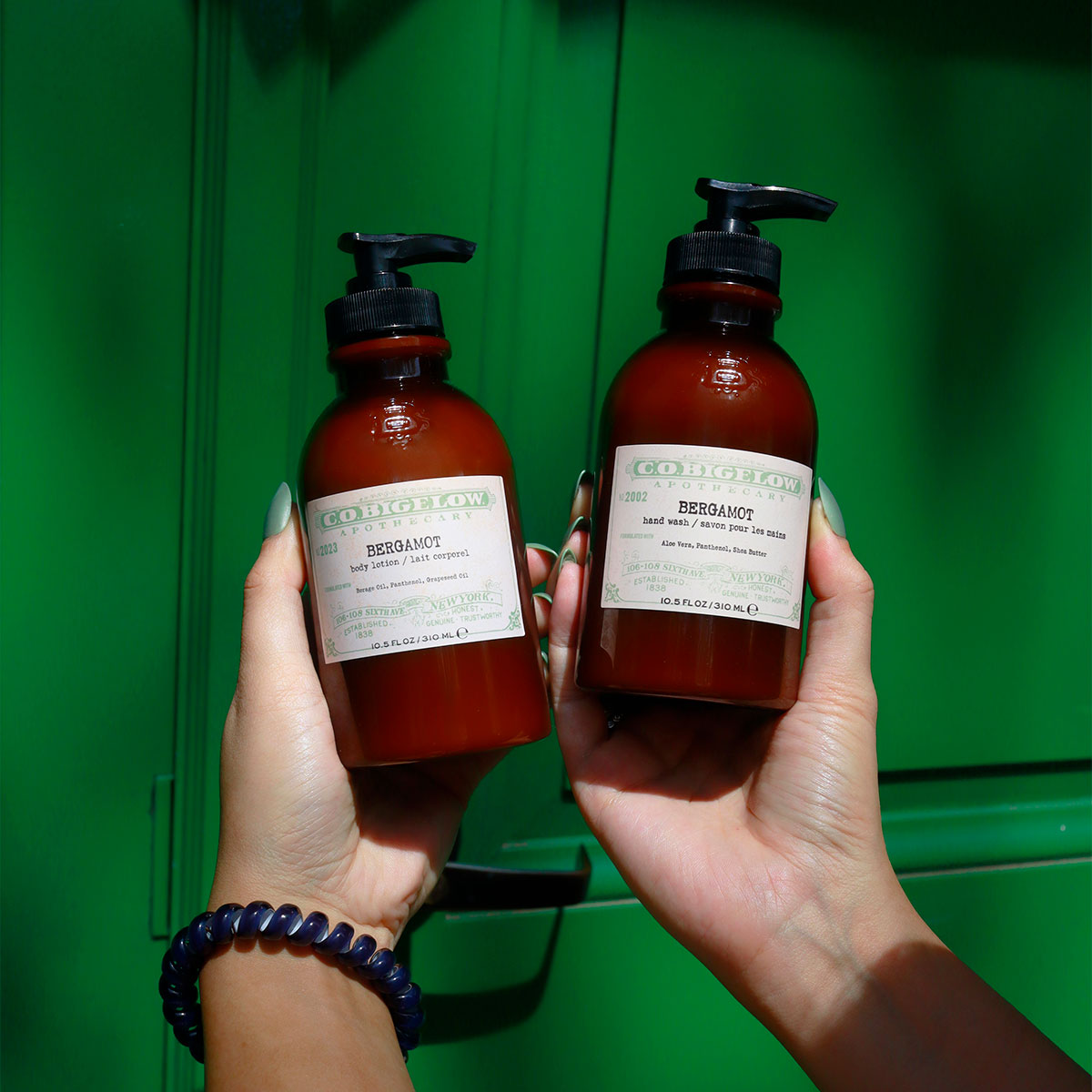 C.O. Bigelow Iconic Collection Bergamot Body Lotion and Hand Wash held in hands in front of a green door. 