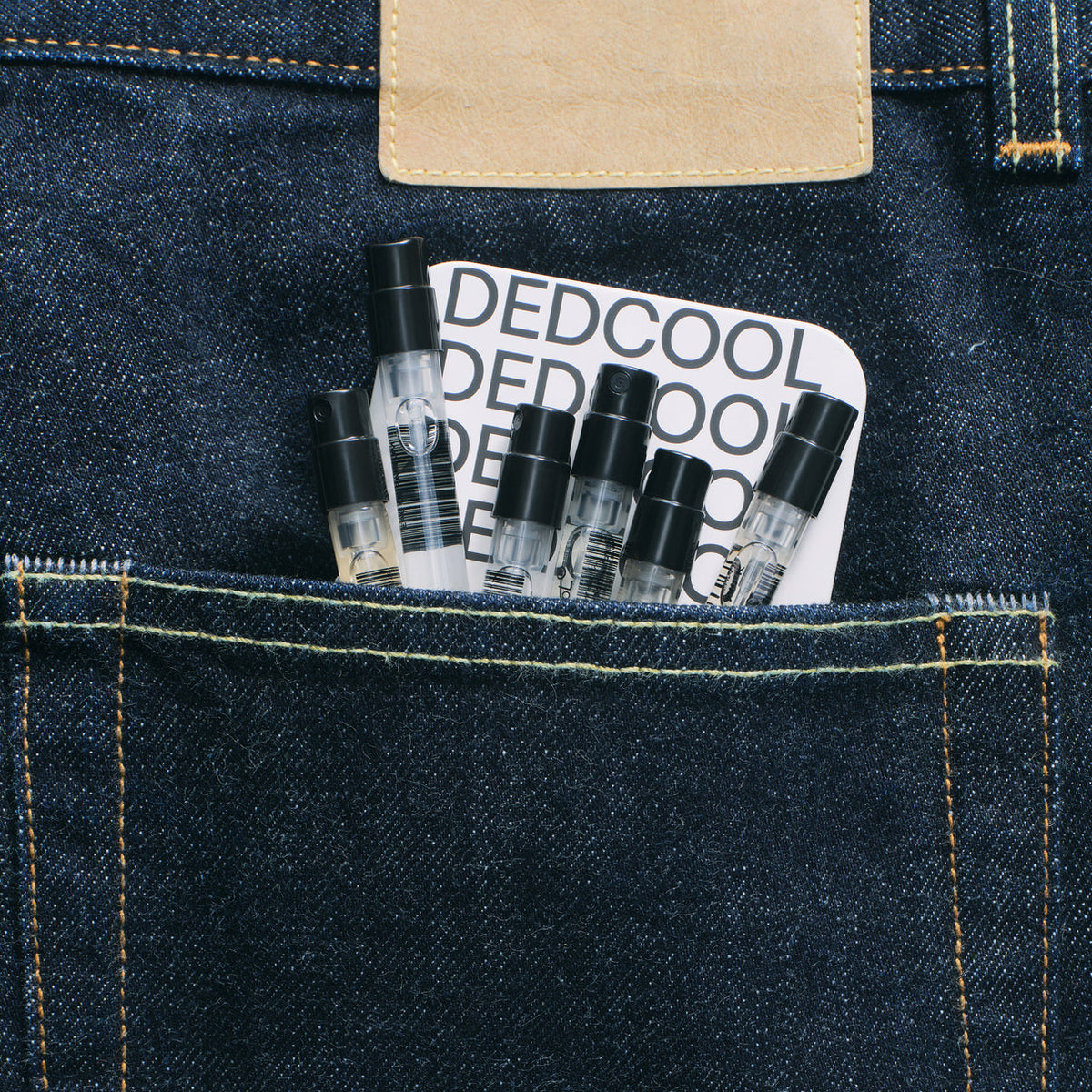 Small bottles of perfume or cologne in a denim pocket with 'DEDCOOL' branding.