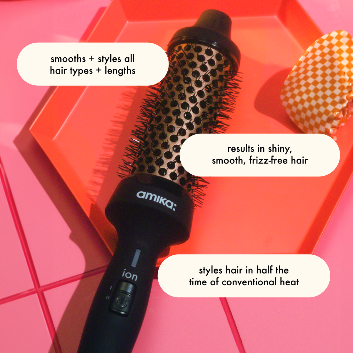 Amika Blowout Babe Hairbrush tool with product details text on a pink and orange geometric background