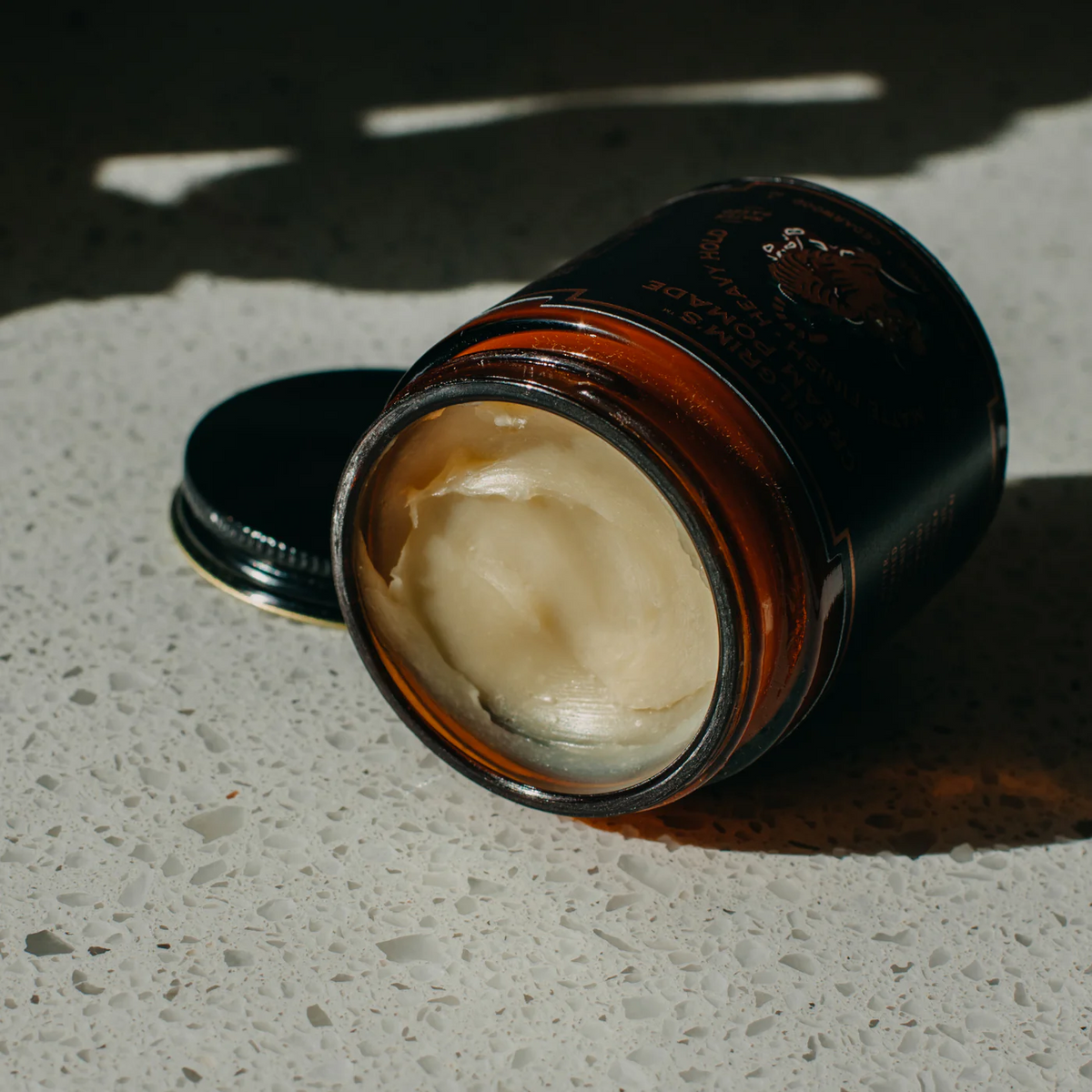 Jar of cream on a textured surface with a dark lid