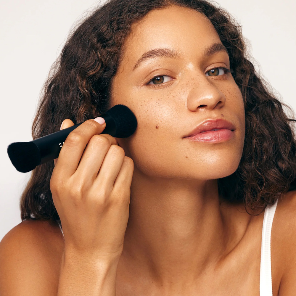 Woman with a brush on her face, on a plain background