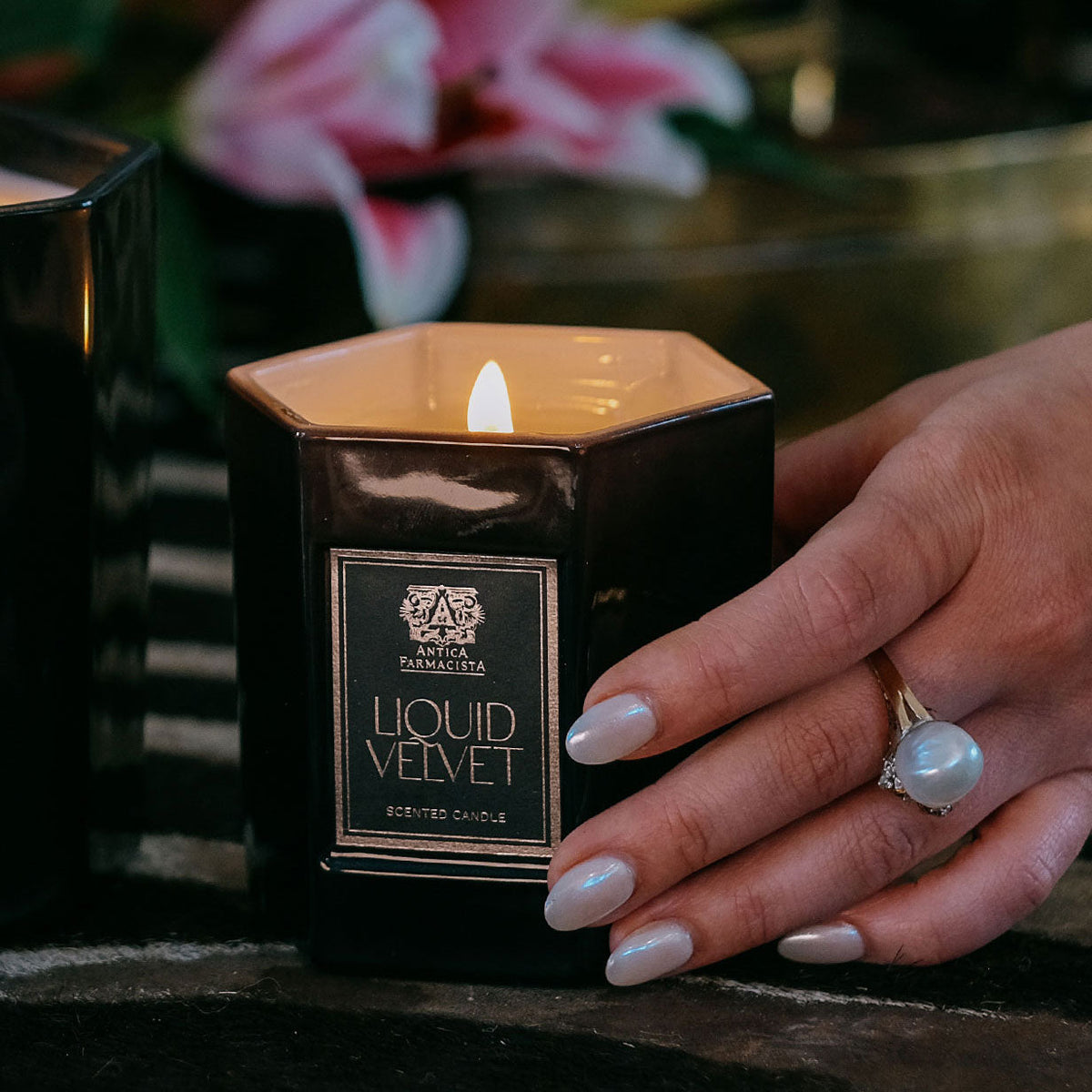 Hand holding Liquid Velvet candle with flower in the background